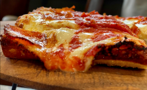 Close-up of a slice of pizza with melted cheese and pepperoni on a wooden serving board.