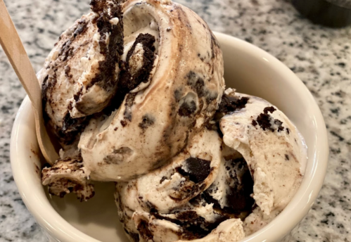 A bowl of swirled chocolate and vanilla ice cream with cookie pieces, topped with a wooden spoon.