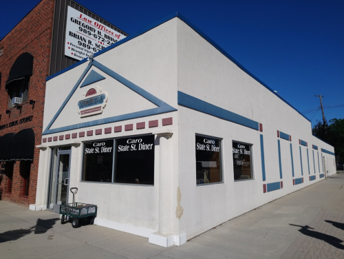 Exterior of a diner with a white facade, blue accents, and large windows displaying the name "Caro State St. Diner."