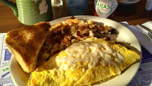 A plate of breakfast featuring an omelette with sauce, hash browns, toast, and a bottle of Tabasco sauce.