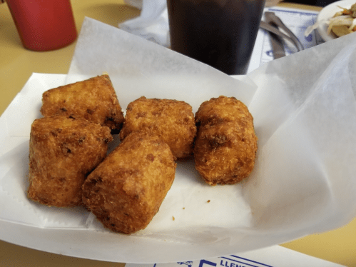 A basket of five golden-brown, crispy tater tots on a white paper liner.