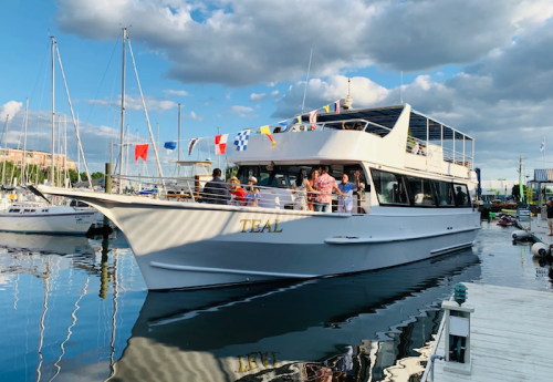 A large white boat named "Teal" docked at a marina, with people on board and colorful flags decorating the top.