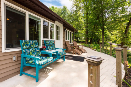 A cozy outdoor seating area with colorful chairs, a wooden deck, and lush greenery in the background.