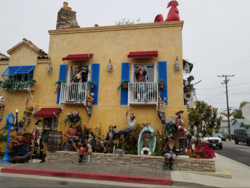Colorful building with blue shutters, adorned with various whimsical sculptures and flowers outside.