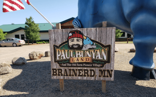 Sign for Paul Bunyan Land in Brainerd, MN, featuring a colorful design and a large blue statue of Paul Bunyan nearby.