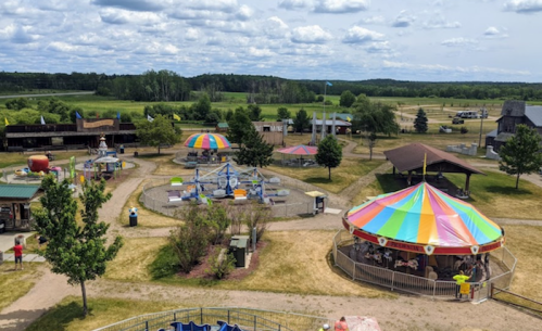 A colorful amusement park with a carousel, playground, and picnic areas under a partly cloudy sky.