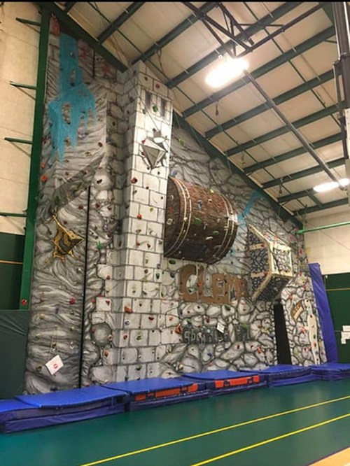 Indoor climbing wall featuring a barrel design, colorful holds, and a padded landing area in a gym setting.