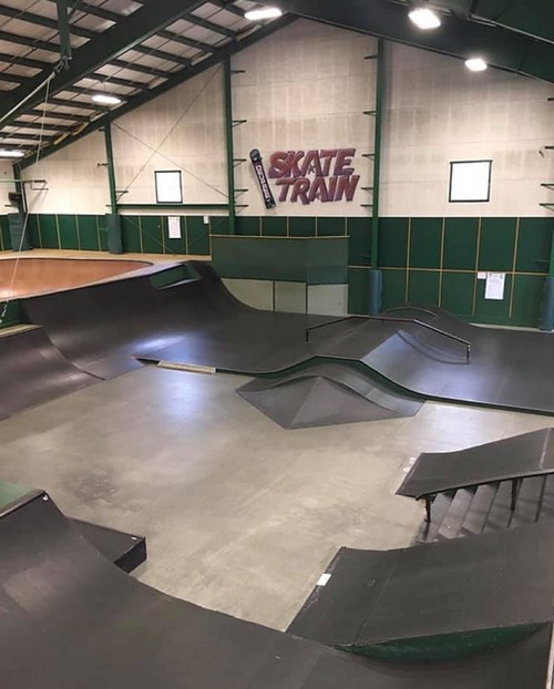 Indoor skate park featuring ramps, rails, and a large bowl area, with "Skate Train" sign on the wall.