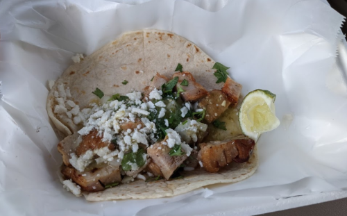 A tortilla filled with grilled chicken, green salsa, cheese, and cilantro, served with a lime wedge.
