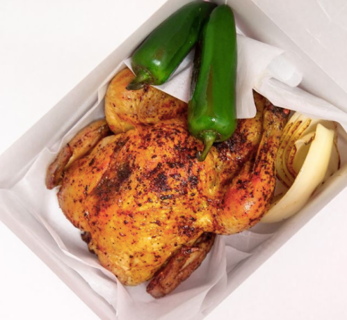 A roasted chicken in a box, accompanied by two green jalapeños and a banana, all on white parchment paper.