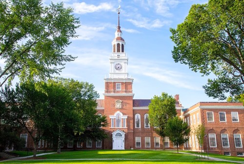 Historic brick building with a clock tower, surrounded by green trees and a clear blue sky.