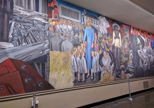A colorful mural depicting a historical scene with people, machinery, and agricultural elements in a dynamic composition.