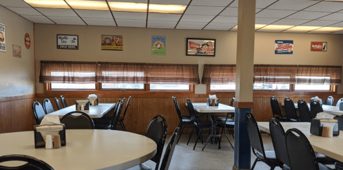 A cozy diner interior with tables, chairs, and vintage signs on the walls, featuring large windows with brown curtains.