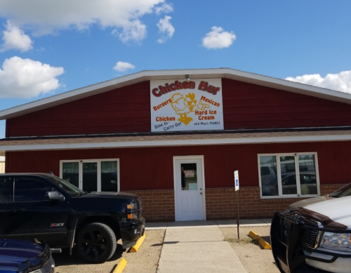 A red building with a sign reading "Chicken Hut" offering burgers, Mexican food, chicken, and ice cream.