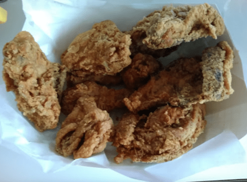 A basket of crispy fried chicken pieces arranged on white paper.