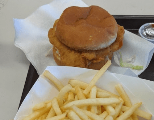 A crispy chicken sandwich on a bun with lettuce, served with a side of golden French fries and dipping sauce.