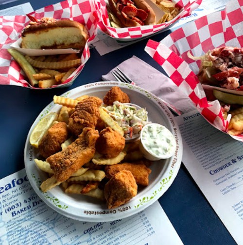A plate of fried seafood with fries and coleslaw, accompanied by two sandwiches and more fries in the background.