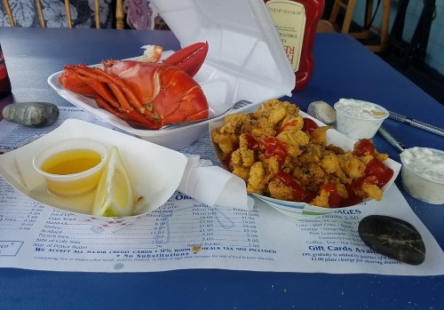 A table with a lobster, fried seafood, dipping sauces, and a menu, set against a casual dining backdrop.