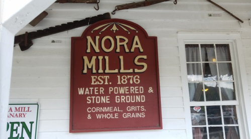 Sign for Nora Mills, established in 1876, highlighting water-powered stone ground cornmeal, grits, and whole grains.