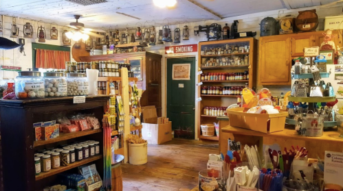 A cozy, vintage store filled with jars, canned goods, and various items on wooden shelves and tables.