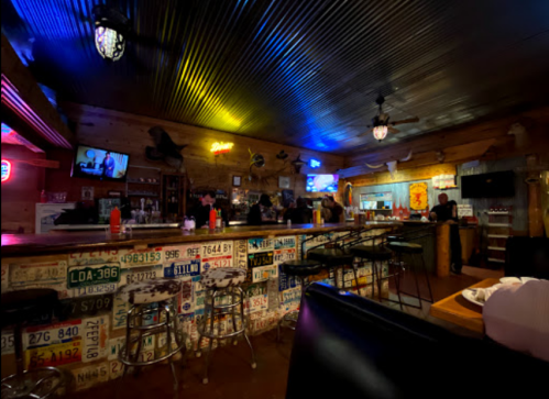 A cozy bar interior with colorful lights, wooden walls, and a wall decorated with license plates.