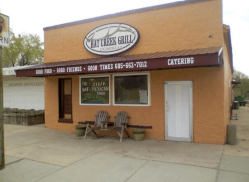 Exterior of Hat Creek Grill, featuring a sign with restaurant details and two wooden chairs on the porch.