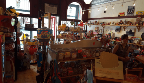 A colorful vintage shop filled with toys, candy, and souvenirs, with a woman browsing in the background.