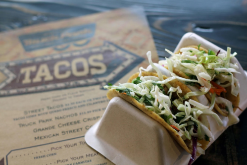 A close-up of a taco filled with shredded cabbage and meat, next to a menu featuring taco options.