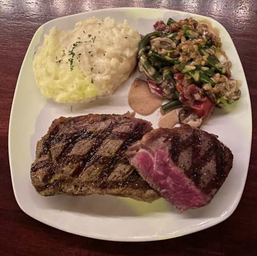 A plate with grilled steak, creamy mashed potatoes, and a vegetable medley with nuts and sauce.