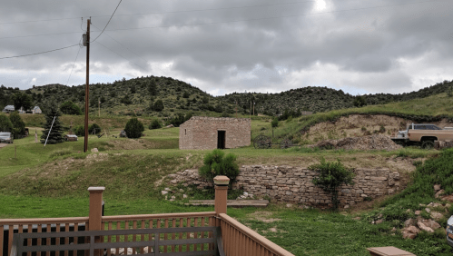 A rural landscape featuring a stone building, grassy hills, and a parked truck under a cloudy sky.