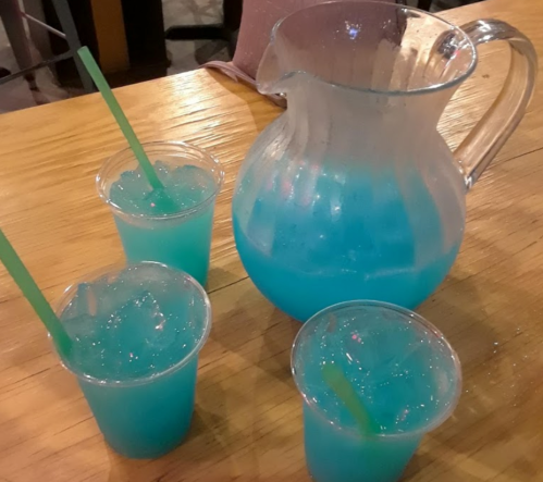 A pitcher and three cups filled with bright blue drinks, all on a wooden table.
