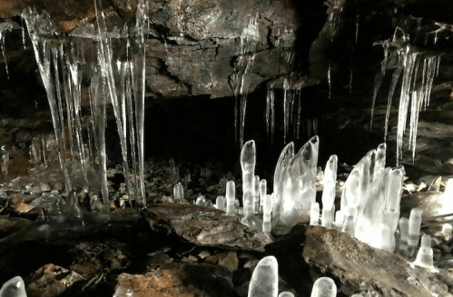 Stalactites and ice formations in a dark cave, with shimmering icicles and rocky ground.
