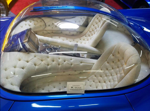 A blue vintage car with a transparent roof showcasing plush, tufted white seats and a sleek dashboard.
