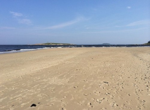 A sandy beach with gentle waves, under a clear blue sky, and distant islands visible on the horizon.