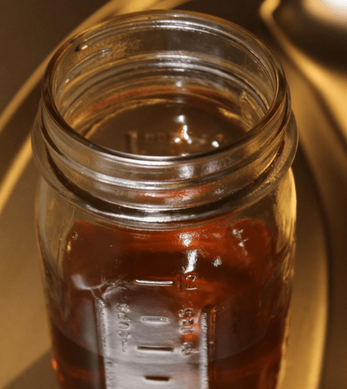 A close-up of a glass jar filled with a dark liquid, resting on a metallic surface.