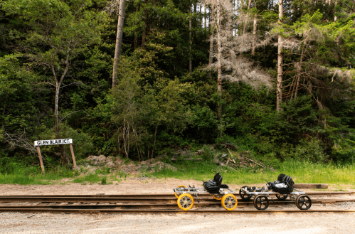 Two railway carts sit on tracks near a sign that reads "GLEN BLAIR JCT." surrounded by lush greenery and trees.