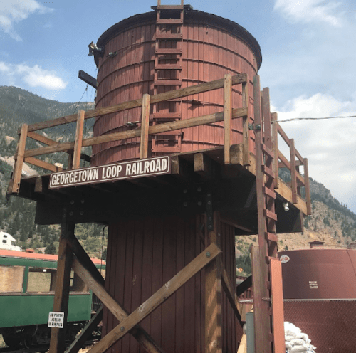 A red wooden water tower with a sign reading "Georgetown Loop Railroad," set against a mountainous backdrop.
