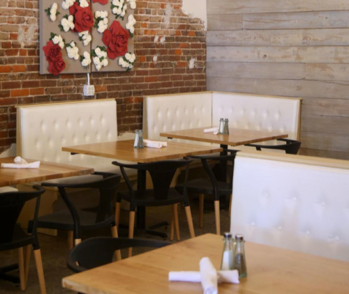 Cozy restaurant interior with wooden tables, white tufted seating, and a floral wall decoration.
