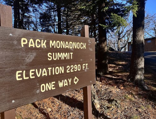 Sign for Pack Monadnock Summit, indicating an elevation of 2290 ft and a one-way direction. Surrounded by trees.