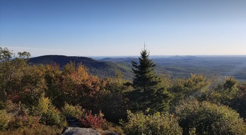 A scenic view of rolling mountains and colorful autumn foliage under a clear blue sky.