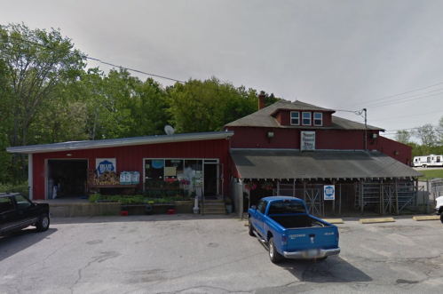 A red building with a sign reading "Blue's" and a blue truck parked outside, surrounded by greenery.