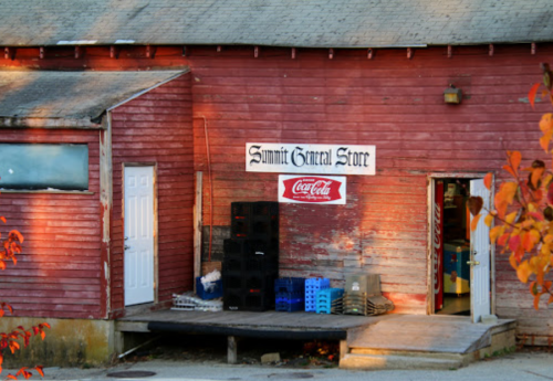 Exterior of Summit General Store, featuring a red wooden building and Coca-Cola signage, with crates stacked outside.