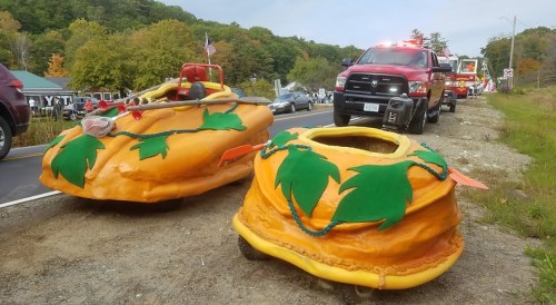 Two colorful, oversized inflatable burger-shaped floats parked by a road, with emergency vehicles in the background.