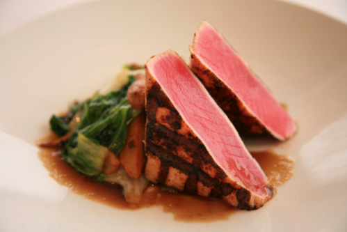 Seared tuna steak slices on a bed of sautéed greens and mushrooms, drizzled with a savory sauce.