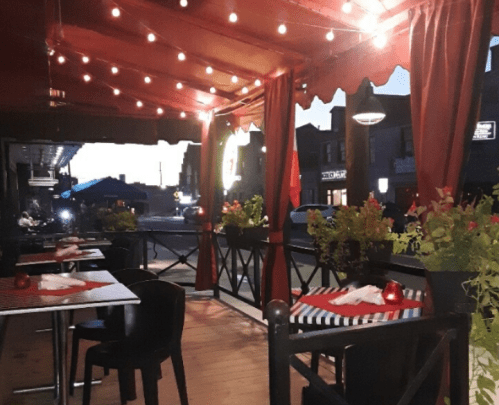 Cozy restaurant patio with string lights, potted plants, and tables set for dining at dusk.