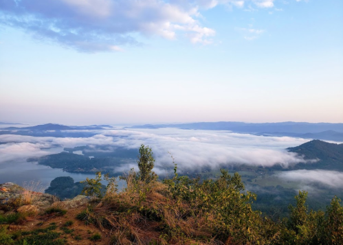 A scenic view of mountains and valleys shrouded in mist under a blue sky with soft clouds.