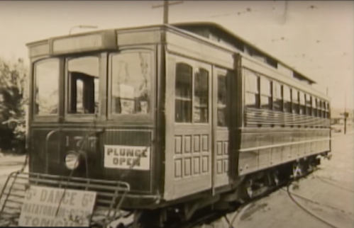 Historic streetcar with a sign reading "Plunge Open" parked on tracks, showcasing vintage design and architecture.