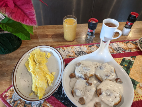 A plate with an omelet, a dish of biscuits and gravy, a glass of orange juice, and a cup of coffee on a colorful tablecloth.