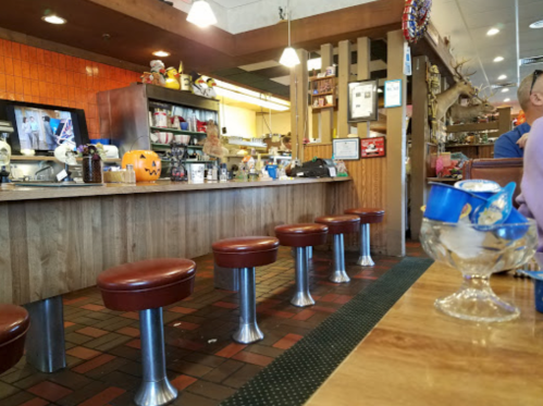 A cozy diner interior with red stools, a counter, and Halloween decorations, featuring a pumpkin and a dessert bowl.
