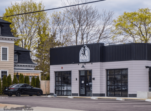 A modern building with a sign reading "Hucks," surrounded by trees and parked cars on a cloudy day.